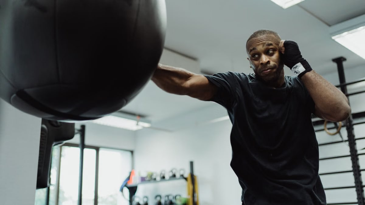 Boxer in black shirt intensely punching a heavy bag during training indoors.